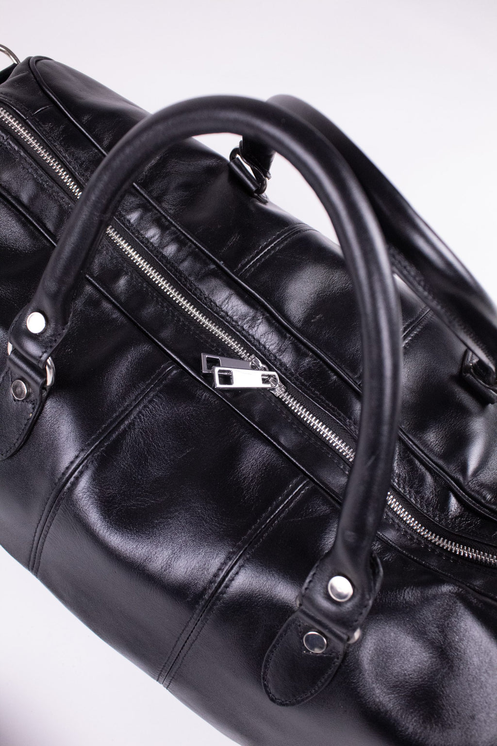 Black genuine leather travel bag with sturdy handles and visible stitching, suitable for stylish journeys.
